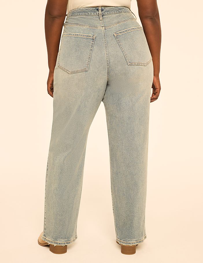 A person wearing light-wash denim jeans stands against a plain, peachy-pink background.