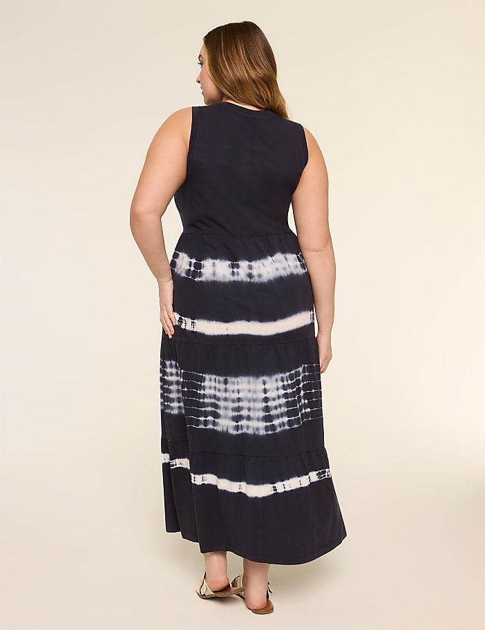 A woman in a dark blue tie-dye maxi dress stands against a plain, light-colored background.