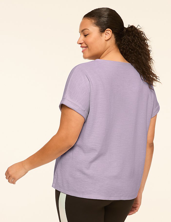 A woman in a light purple t-shirt and black leggings with a stripe stands against a plain, light-colored background.