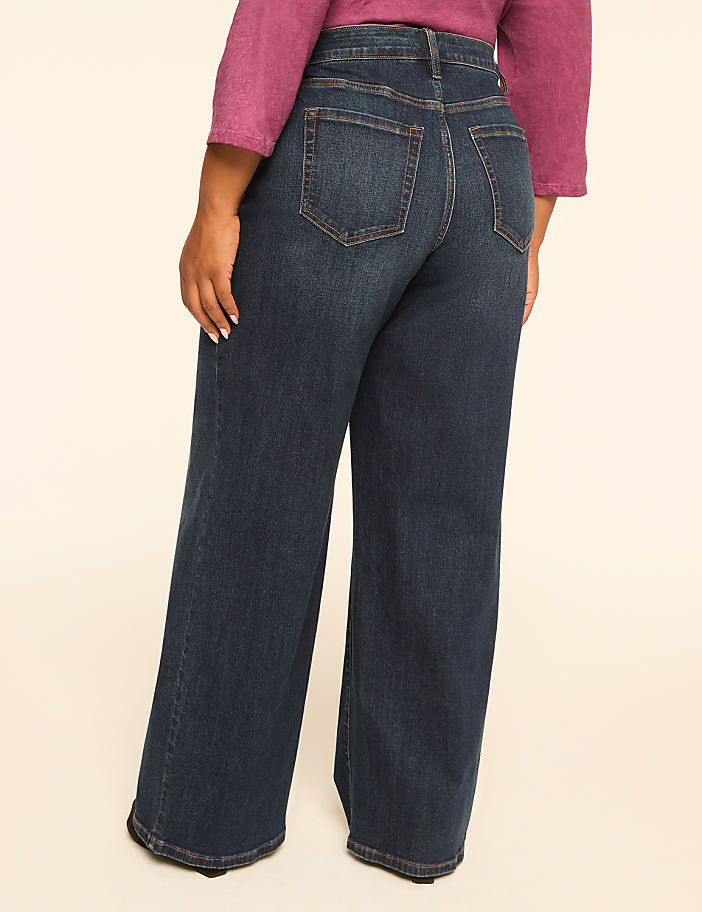 A person wearing dark wash wide-leg jeans stands against a plain, light-colored background.