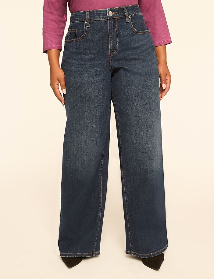 A person wearing dark wash wide-leg jeans stands against a plain, light-colored background.