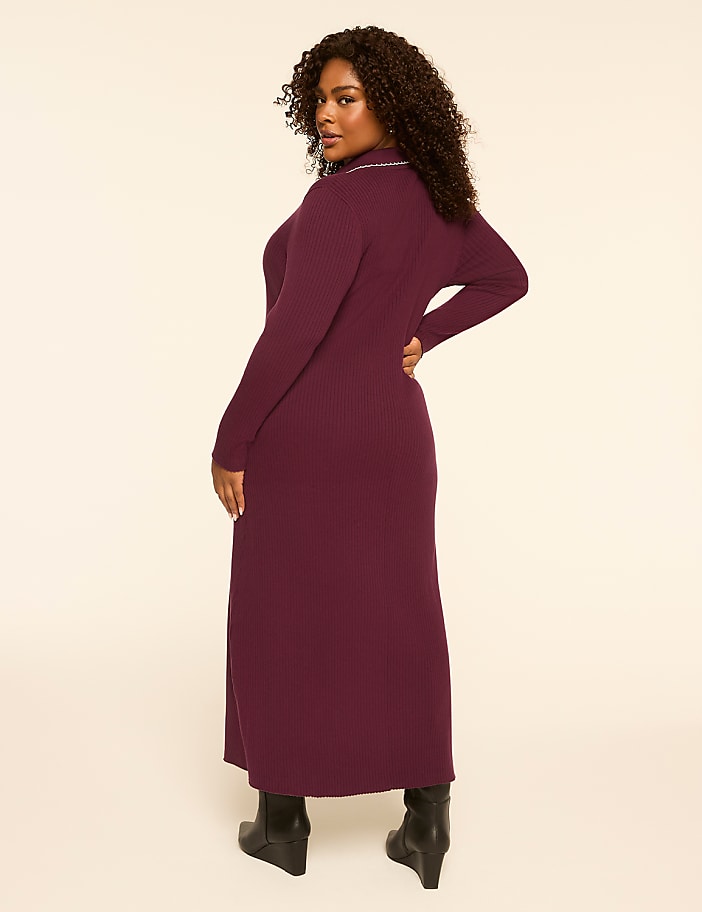 A woman in a burgundy ribbed dress and black boots stands against a plain, light-colored background.