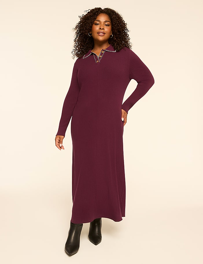 A woman in a burgundy ribbed dress and black boots stands against a plain, light-colored background.