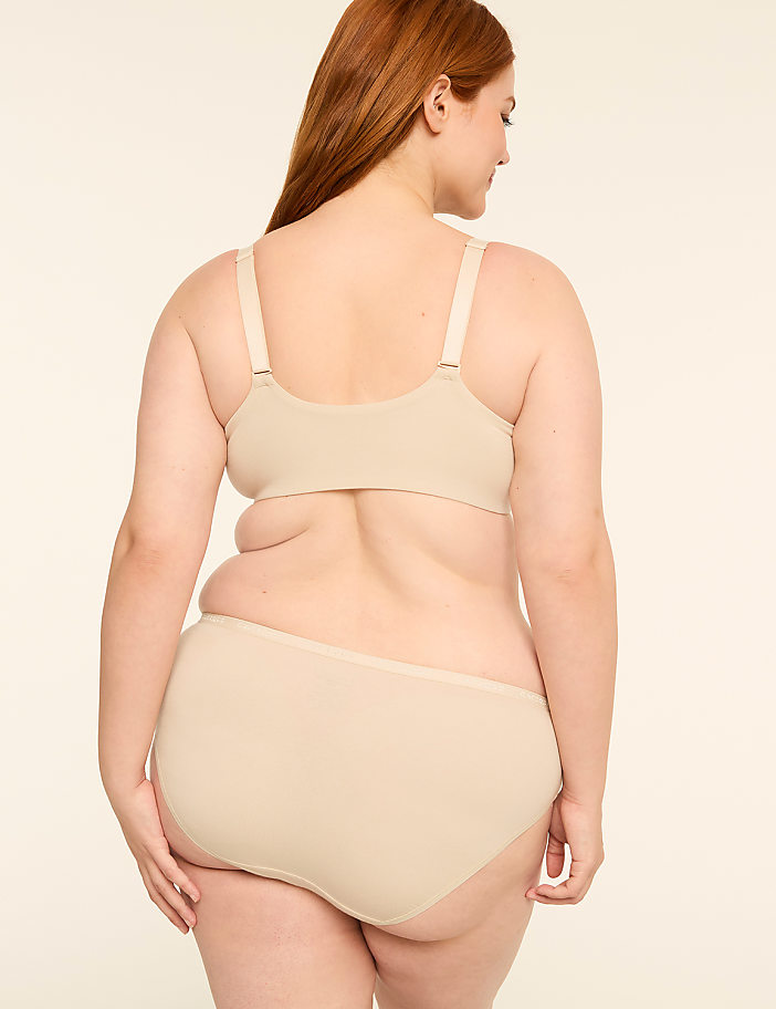 A woman in beige undergarments stands with her back to the viewer against a plain, light-colored background.