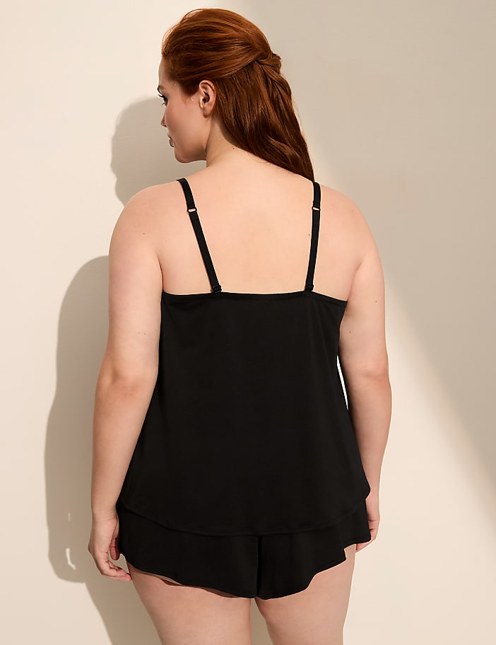 A woman in black sleepwear stands against a plain, light-colored wall with a shadow cast behind her.