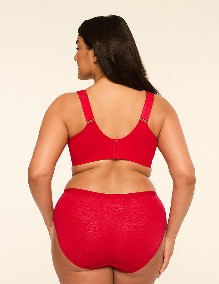 A woman in a red bra and matching patterned underwear stands against a plain, light-colored background.