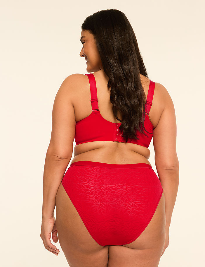 A woman in red lingerie stands against a plain, light-colored background.