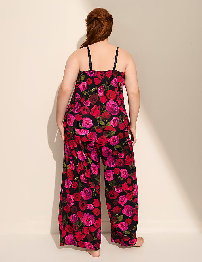 A woman in a floral pajama set stands against a plain, light-colored wall with a shadow cast on it.