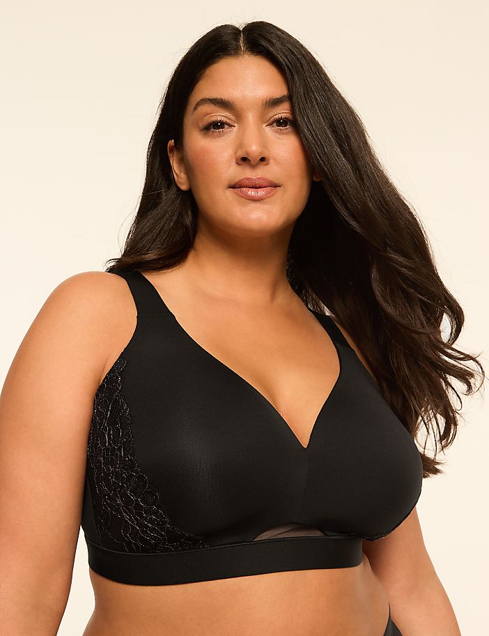 A woman with long dark hair wears a black bra with lace detailing on the side, against a plain, light-colored background.