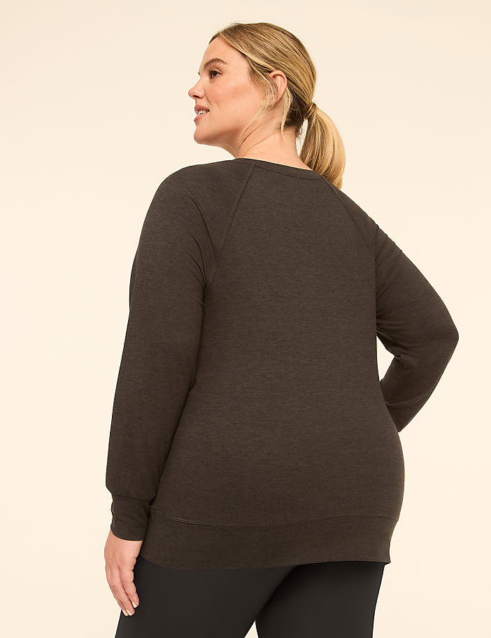 A woman in a dark grey sweatshirt and blue plaid pants stands against a plain, light-colored background.