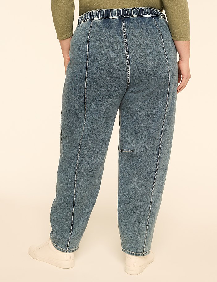 A person wearing loose-fitting denim pants stands against a plain, light-colored background.