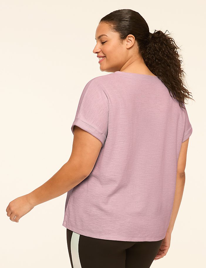 A woman in a light purple t-shirt and black leggings with a stripe stands against a plain, light-colored background.
