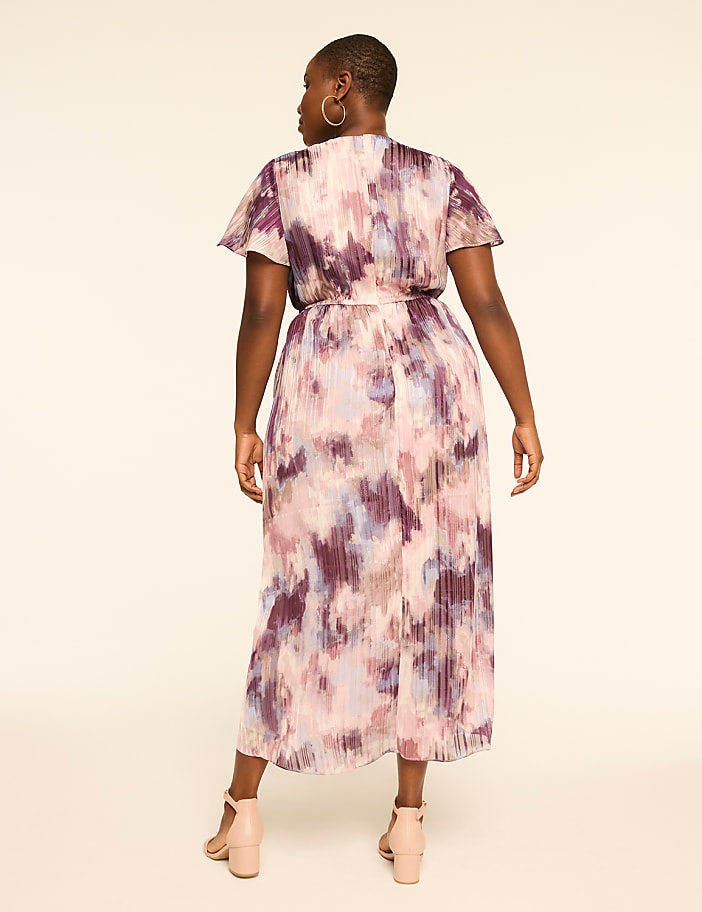 A woman in a floral-patterned dress stands against a plain, light-colored background.