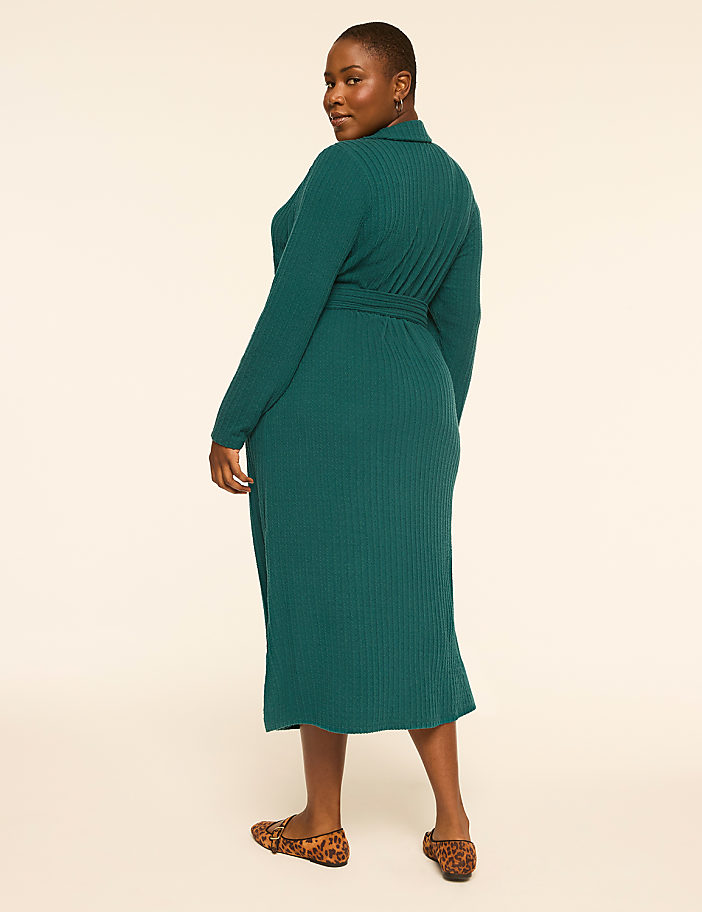 A woman in a teal ribbed dress and leopard print flats stands against a plain cream background.