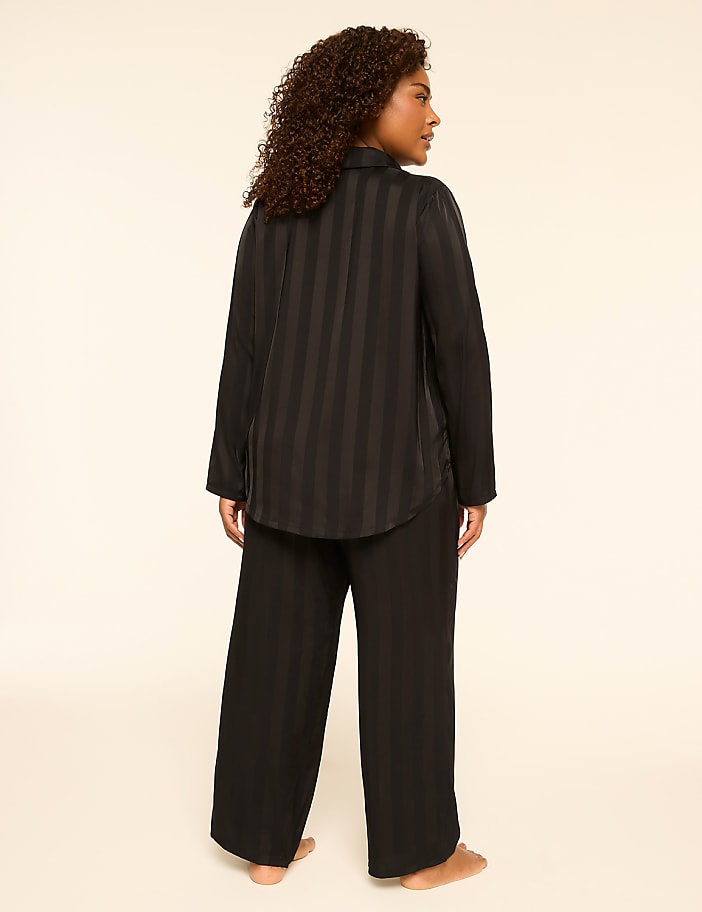 A woman stands facing away from the camera in black striped pajamas against a plain, light-colored background.