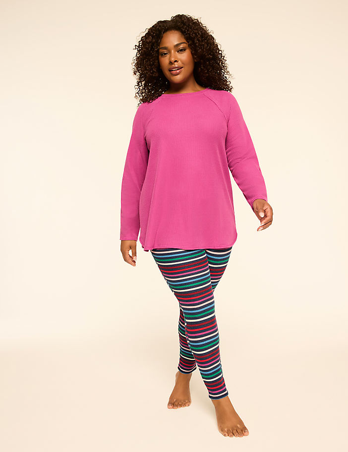 A woman in a pink tunic and striped leggings stands against a plain, light-colored background.