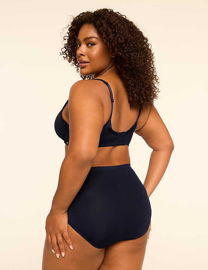 A woman in navy blue lingerie stands against a plain, light-colored background.