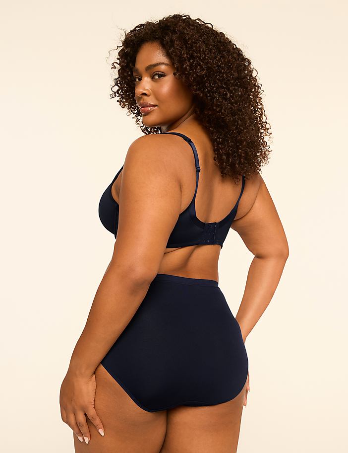 A woman in navy blue lingerie stands against a plain, light-colored background.