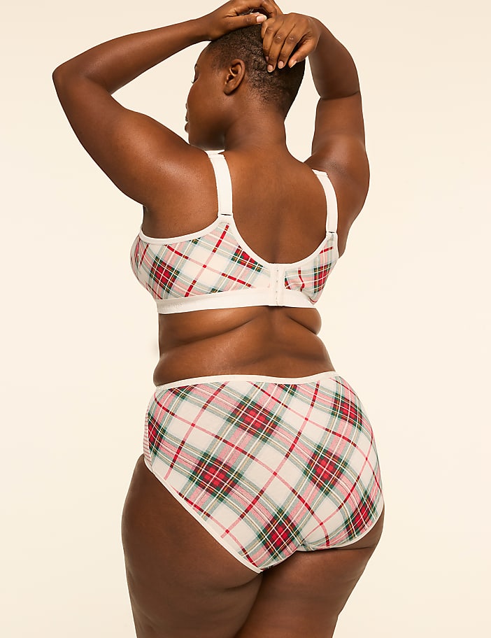 A woman in a plaid bra and underwear stands with her hands behind her head against a plain, light-colored background.