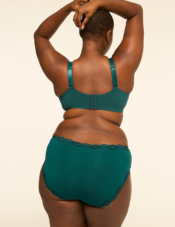 A woman in a teal bra and matching underwear stands with her back to the camera against a plain, light-colored background.