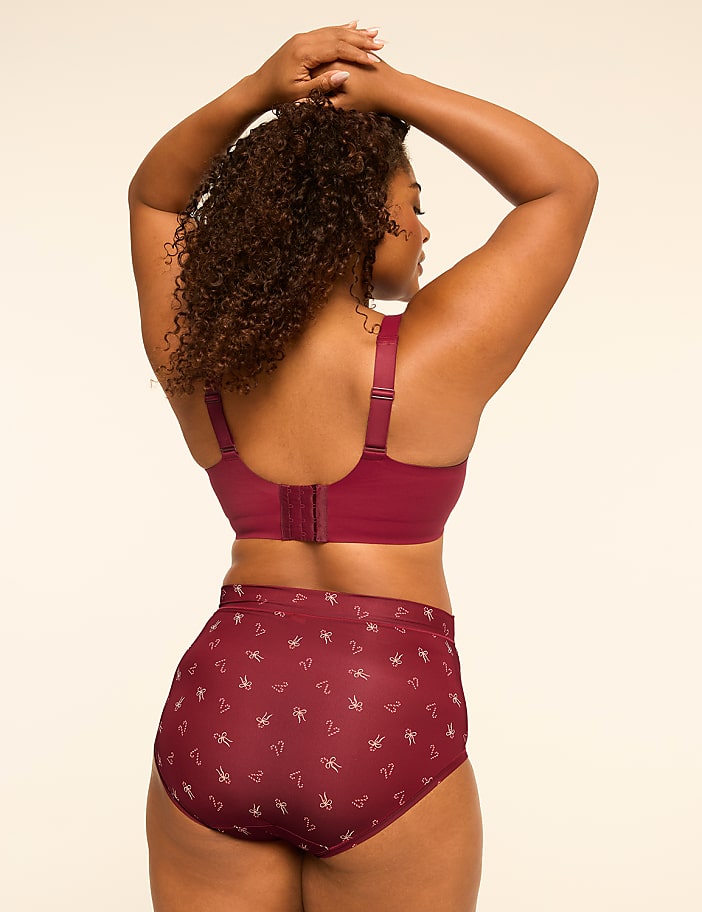 A woman in a maroon bra and matching patterned underwear stands with her back to the viewer against a plain, light-colored background.