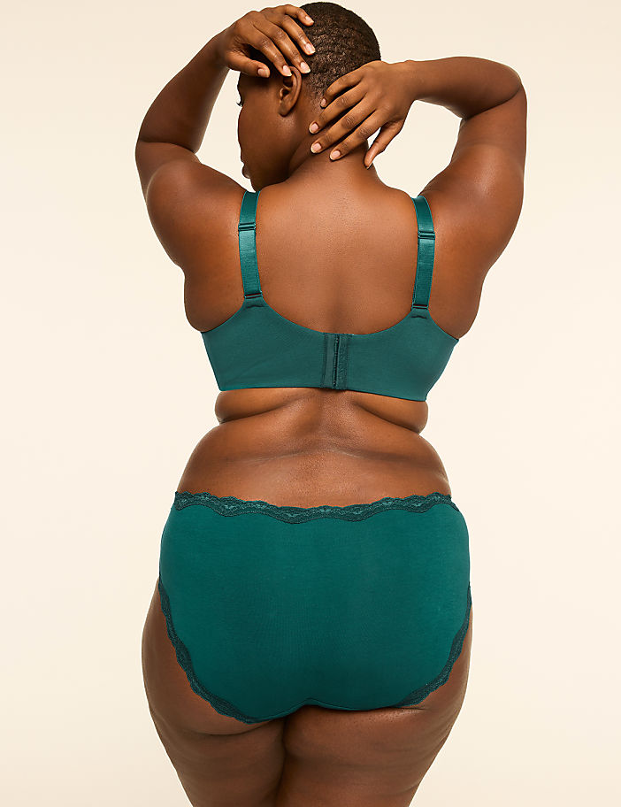 A woman in a teal bra and matching underwear stands with her back to the camera, hands behind her head, against a plain, light-colored background.