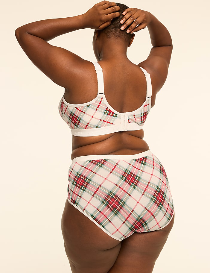 A woman in a plaid bra and underwear stands with her hands behind her head against a plain, light-colored background.