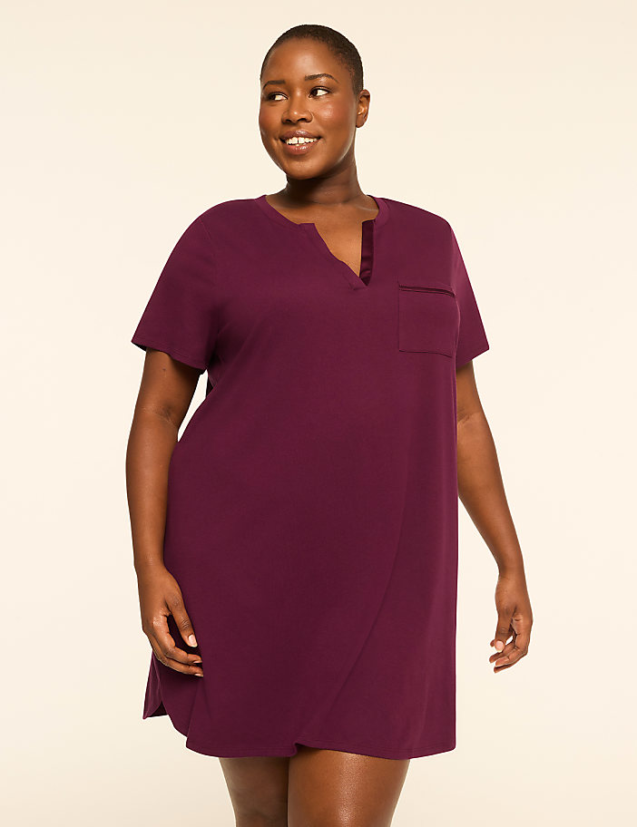 A smiling woman in a plum-colored nightgown stands against a plain, light-colored background.