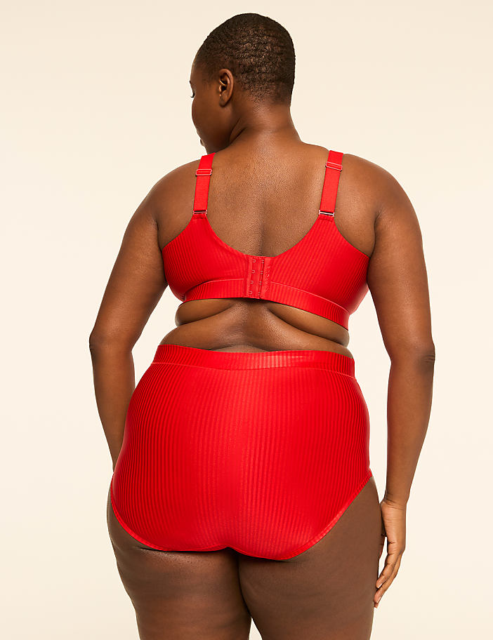 A woman in a red ribbed bra and high-waisted briefs stands against a plain, light-colored background.