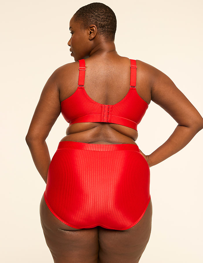 A woman in a red ribbed bra and high-waisted briefs stands against a plain, light-colored background.