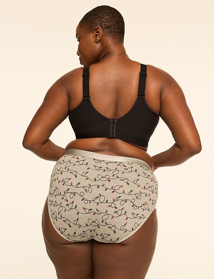 A woman in a black bra and festive patterned underwear stands against a plain, light-colored background.