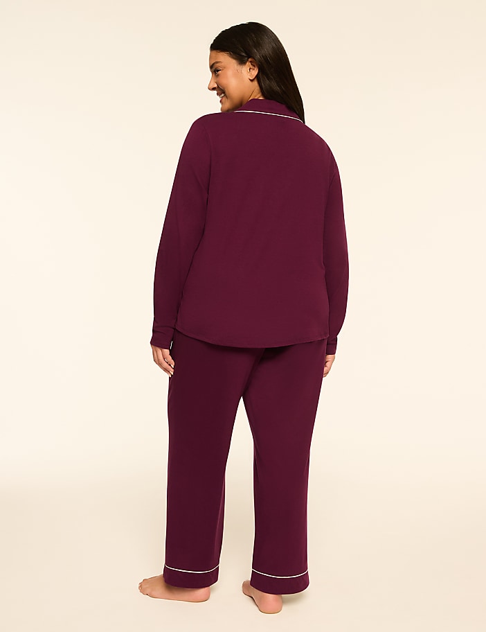 A woman in burgundy pajamas with white piping stands facing away from the camera against a plain, light-colored background.