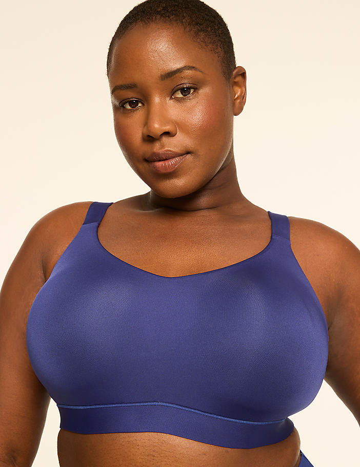 A woman with short hair and a confident expression wears a blue sports bra against a plain, light-colored background.