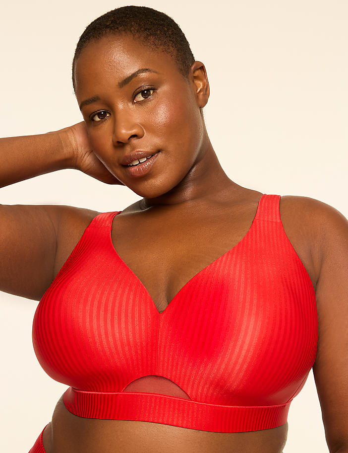 A woman with short hair and a red ribbed bra with a cutout in the front poses against a plain, light-colored background.