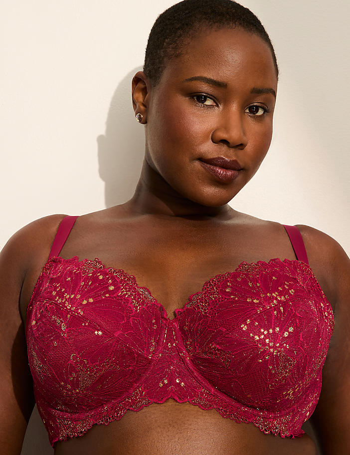 A woman with dark skin and short hair wears a burgundy lace bra in the foreground, against a plain, light-colored background.