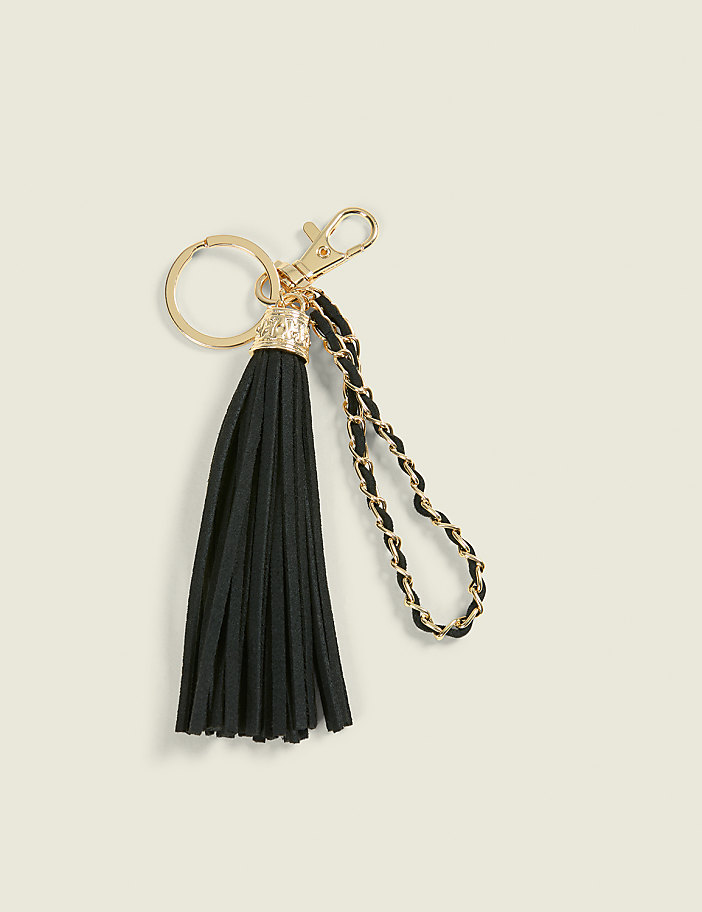 A black tassel keychain with gold hardware and a braided chain strap rests on a light beige background.