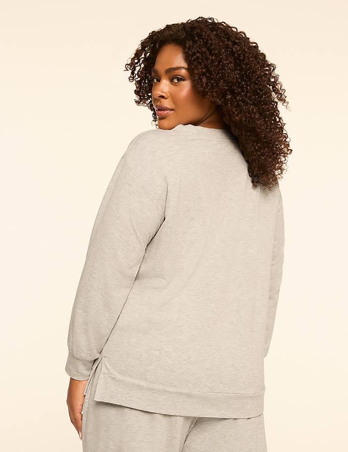 A woman with curly brown hair wearing a gray sweatshirt and sweatpants is shown from the back, looking over her shoulder against a plain, light-colored background.