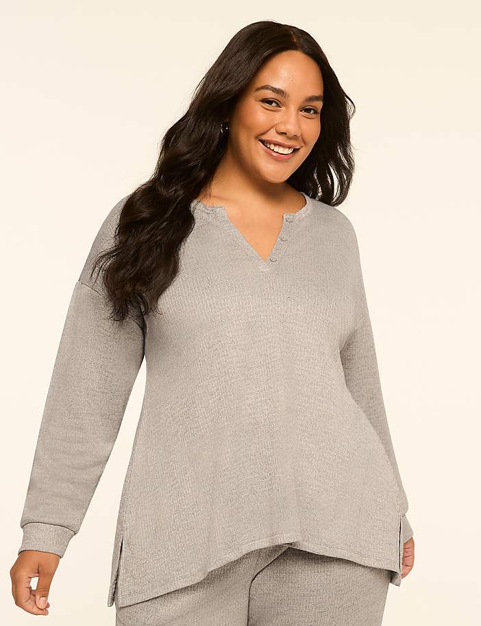 A smiling woman with long, dark hair wears a light gray waffle-knit top and pants against a plain, light beige background.