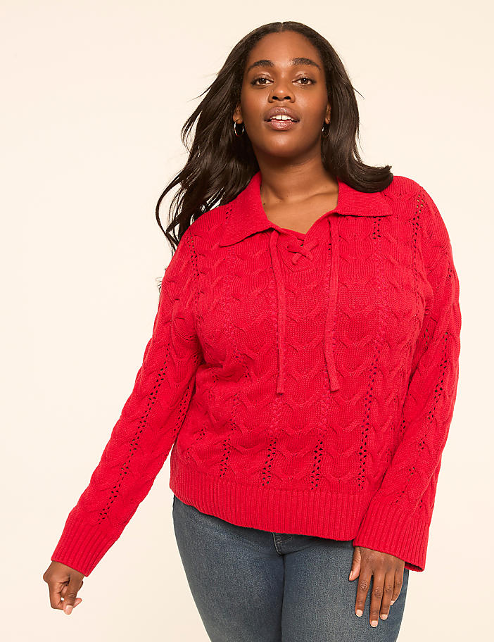 A woman in a red cable-knit sweater and blue jeans stands against a plain, light-colored background.