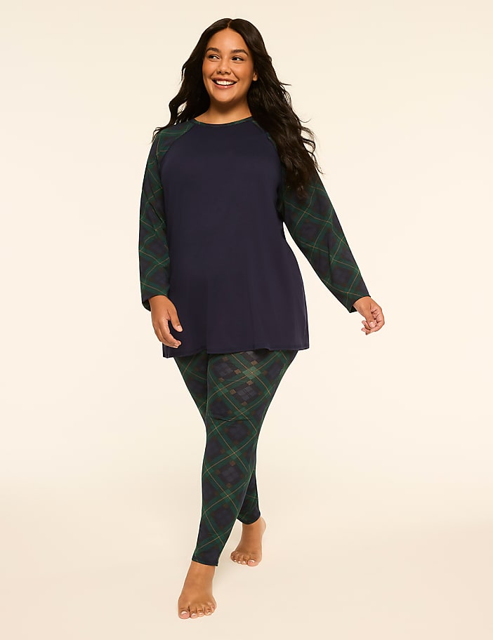 A smiling woman in a navy blue top and plaid leggings stands against a plain, light-colored background.