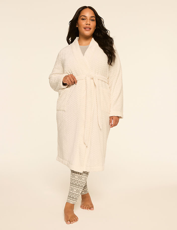 A woman in a cream robe and patterned leggings stands against a plain, light background.