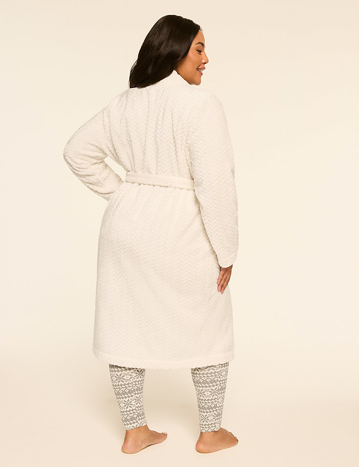 A woman in a white robe and patterned leggings stands against a plain, light-colored background.