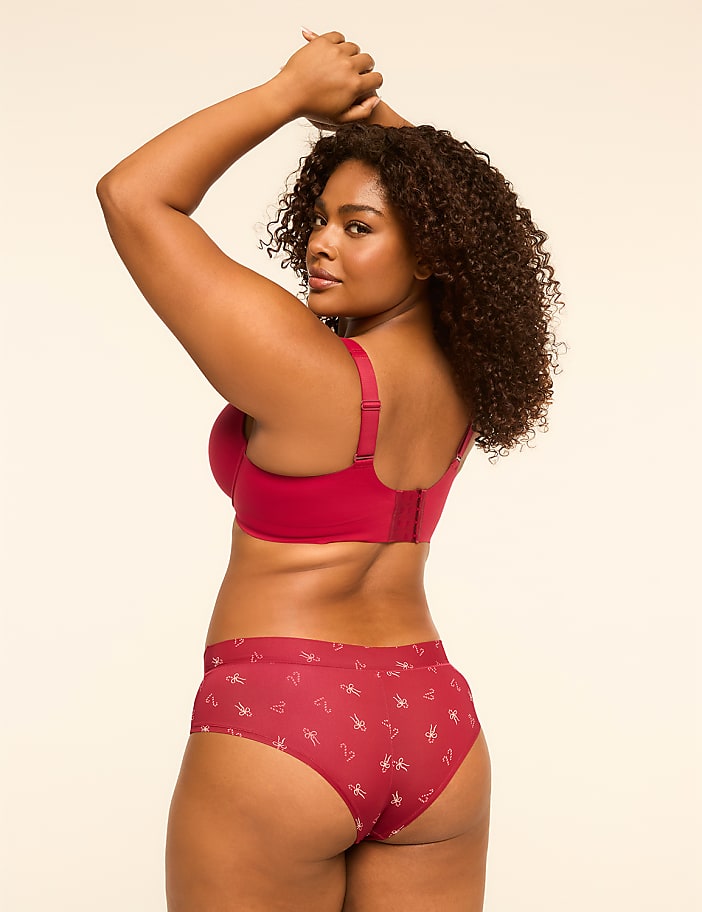 A woman in a red bra and patterned underwear poses with her arms raised against a plain, light-colored background.