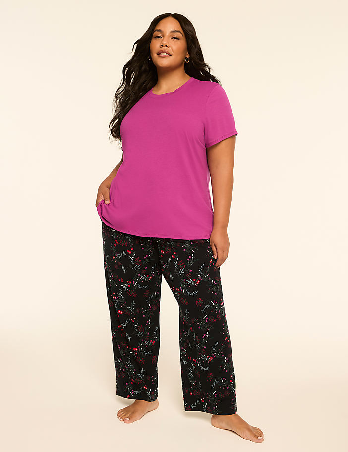 A woman in a magenta t-shirt and patterned pajama pants stands against a plain, light-colored background.