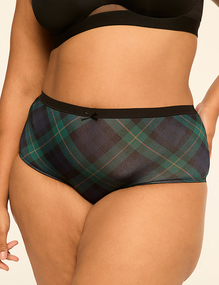 A woman in a black bra and plaid underwear stands against a plain background.