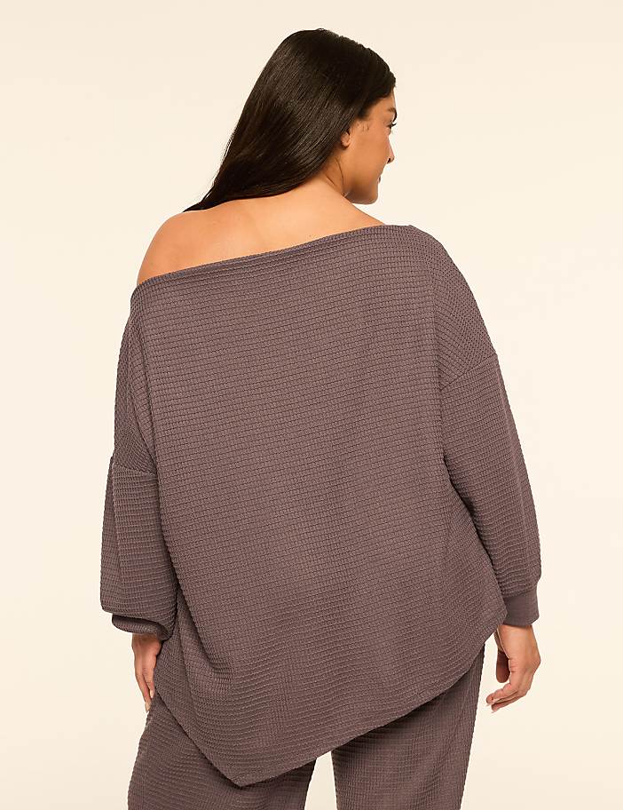 A woman in a textured, off-the-shoulder top and matching pants stands against a plain, light-colored background.