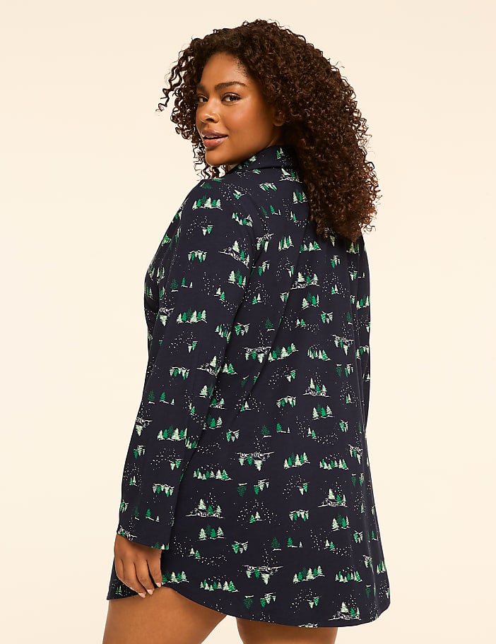 A woman in a dark blue nightgown with a forest print stands against a plain, light-colored background.