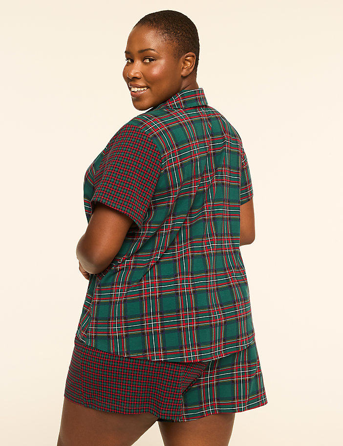 A woman in plaid pajamas smiles over her shoulder against a plain, light background.