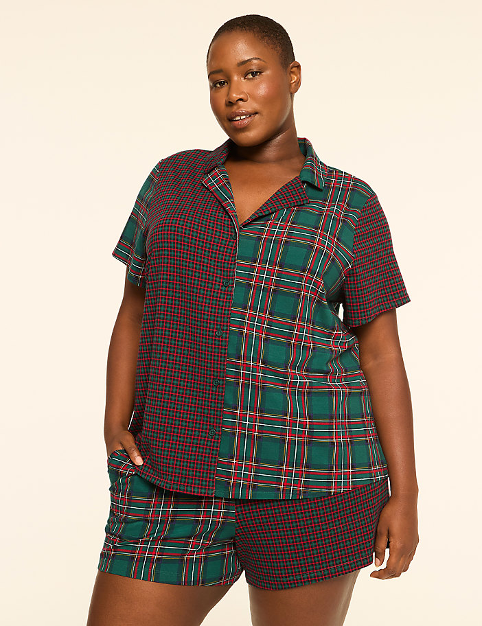 A woman stands in a plain, light-colored studio, wearing a two-toned plaid pajama set.