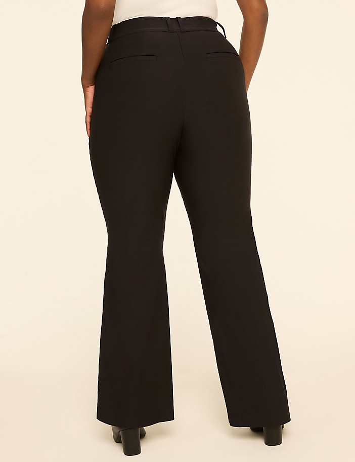 A person wearing black flared pants stands against a plain, light-colored background.